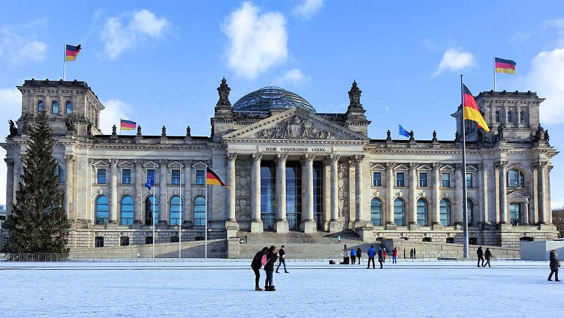 Menschen auf einer Schneefläche vor dem Reichstagsgebäude im Winter. 