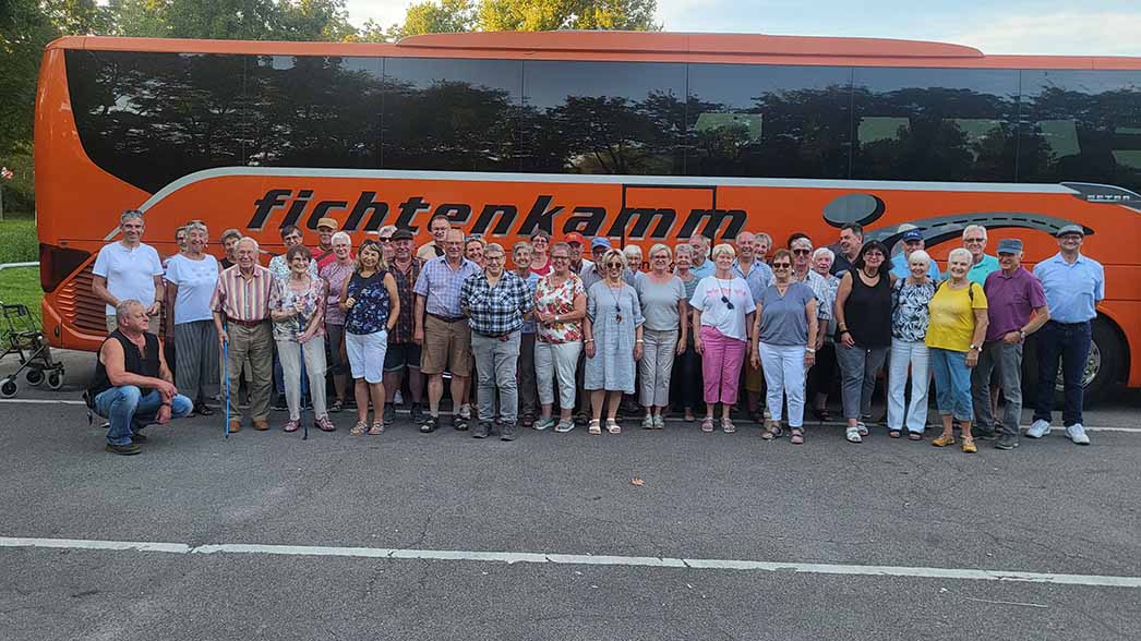 eine große Menschengruppe steht vor einem Reisebus.